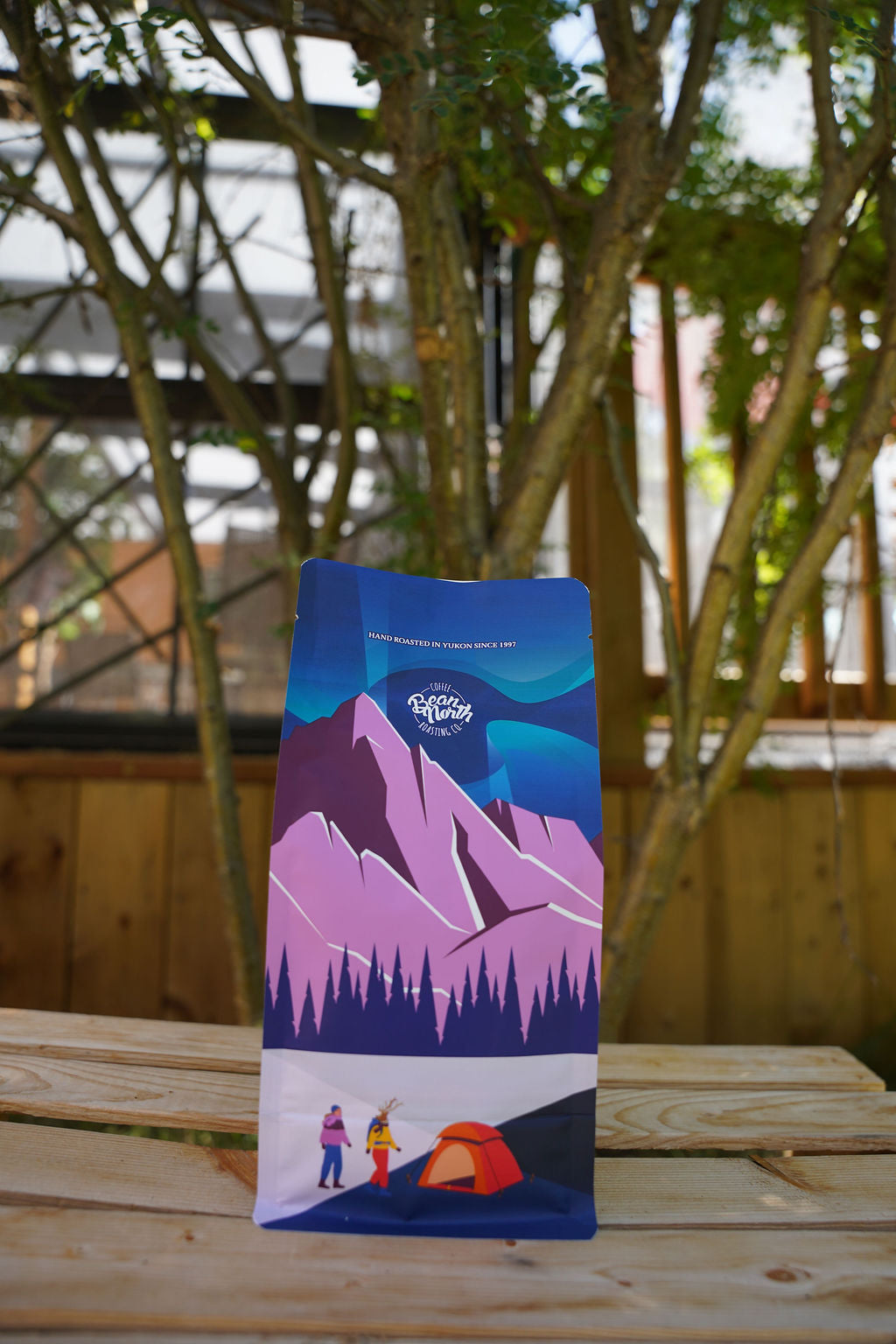 Packaged product with mountain and camping design on a wooden surface with trees in the background
