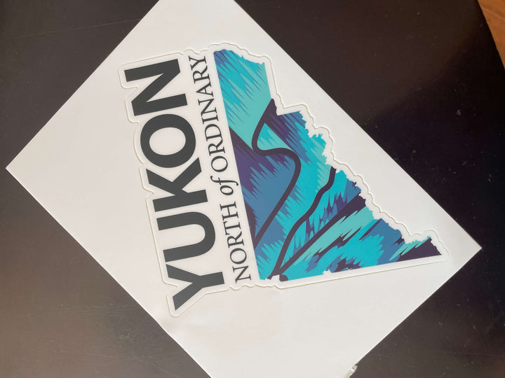 Sticker with 'Yukon North of Ordinary' text and blue and purple northern light graphic on a white background