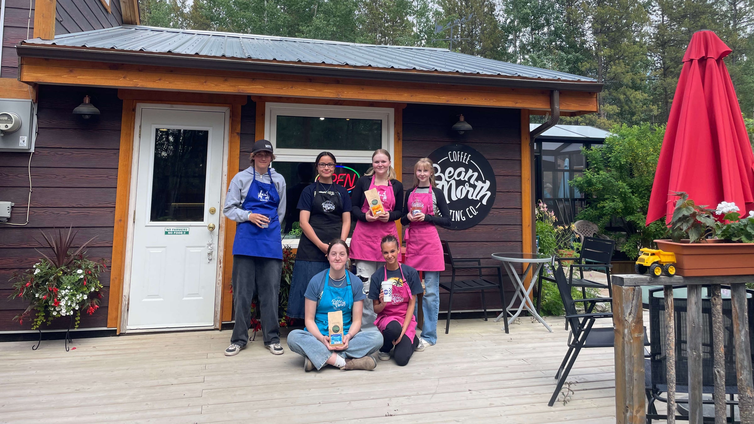 Group of people standing on a wooden deck in front of a small building with a sign.