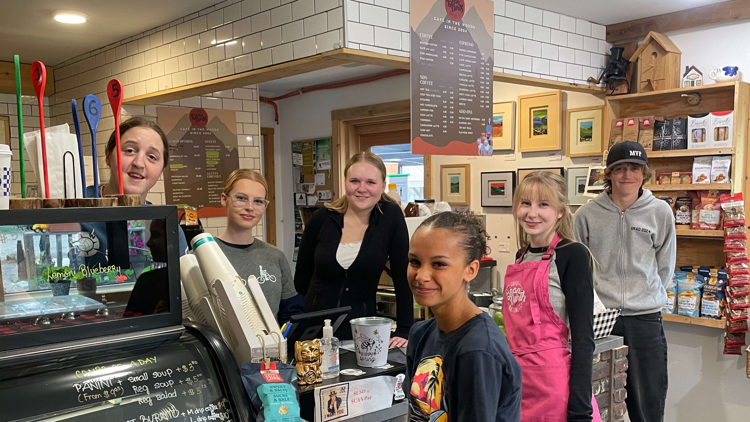 Group of people, including children and adults, standing in a kitchen or diner setting.
